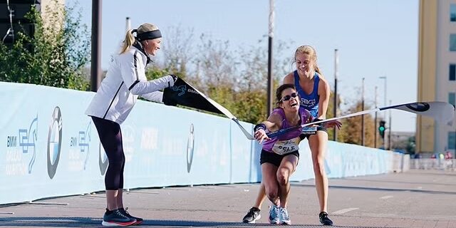 Coureuse épuisée soutenue par une autre à l’arrivée d’un marathon, métaphore du burn-out et du leadership au travail